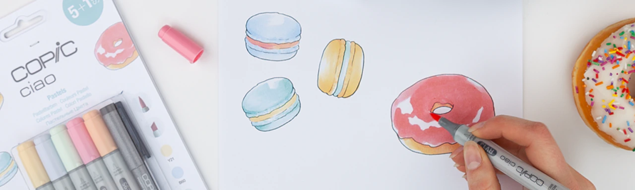 Foto einer Zeichnung einiger bunter Donuts und Macarons mit Hand, die einen Copic Cioa führt